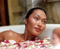 Woman in bathtub with flower petals, water pouring on hair - Jack Hollingsworth
