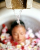 Water pouring on head of woman in bathtub with flower petals - Jack Hollingsworth