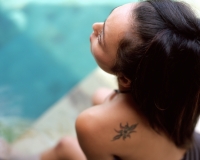 Woman sitting by side of swimming pool, tattoo on shoulder - Jack Hollingsworth