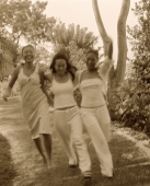 Three women wearing white strolling, holding hands, nature in background - Jack Hollingsworth
