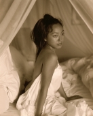 Woman draped in sheet sitting in bed - Jack Hollingsworth