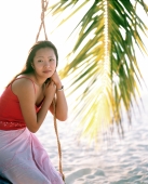 Woman sitting on swing looking off camera, coconut frond in background - Jack Hollingsworth