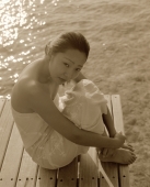 Woman in white dress sitting on dock, water in background, portrait - Jack Hollingsworth