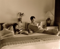 Woman and man in bed reading magazines, tray with cups on bed. - Jack Hollingsworth