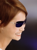 Young woman wearing blue tinted sunglasses, smiling - Eric Ceret