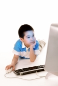 Young boy using desktop computer, looking at monitor, white background. - Jade Lee