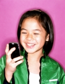 Young girl using cellular phone, smiling, purple background. - Jade Lee