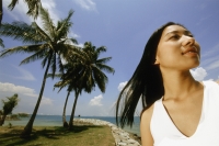 Young woman standing on beach, looking up, coconut trees in background, low angle view - Eric Ceret
