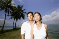 Young couple standing on beach, coconut trees in background, portrait - Eric Ceret