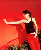 Young woman leaning on wall smiling, red background. - Jack Hollingsworth