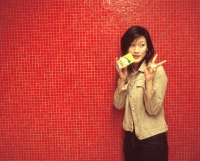Young woman making a peace sign, drinking a packet drink, red background. - Jack Hollingsworth