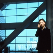 Executive woman using cellular phone indoors, windows in background. - Jack Hollingsworth