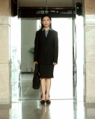Executive woman standing in front of reflective elevator doors, portrait. - Jack Hollingsworth