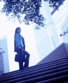 Woman holding bag standing at top of stairs, buildings in background. - Jack Hollingsworth
