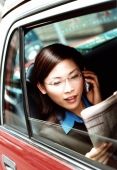 Executive woman using cellular phone and reading newspaper in taxi. - Jack Hollingsworth