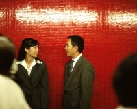 Male and female executives leaning against red wall talking. - Jack Hollingsworth
