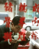 Executive eating bowl of noodles, seen through glass window with Chinese characters. - Jack Hollingsworth