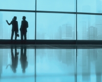 Silhouette of male and female executives by large window, skyline outside. - Jack Hollingsworth