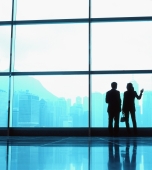 Silhouette of male and female executives by large window, skyline outside. - Jack Hollingsworth