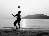 Man playing with football (soccer ball) on beach, silhouette - Jade Lee