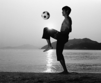 Man playing with football (soccer ball) on beach, silhouette - Jade Lee