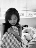 Woman clutching pillow, man sleeping in the background - Jade Lee
