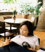 Woman at home reading a magazine, dining room in background - Jade Lee