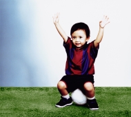 Young boy sitting on soccer ball with arms in the air - Erik Soh