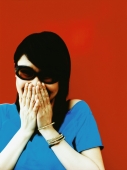 Young woman in sunglasses with hands covering mouth, red background. - Jack Hollingsworth