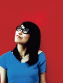 Young woman wearing glasses looking off camera, red background. - Jack Hollingsworth