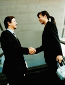 Executive pair shaking hands on escalator. - Jack Hollingsworth