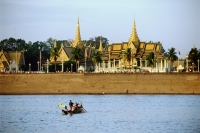 Cambodia, Phnom Penh, Tonle Sap River, Cham fisherman cross river with Royal palace and Silver Pagoda in background. - Steve Raymer