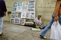 Vietnam, Ho Chi Minh City, A handicapped artist on a sidewalk drawing with his feet. - Steve Raymer