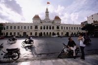 Vietnam, Ho Chi Minh City, Hotel De Ville (People's committee Building), people on motorcycles in foreground. - Steve Raymer