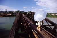 Thailand, Kanchanaburi, River Kwai, A woman crossing the bridge with an umbrella to shield her from the sun. - Steve Raymer