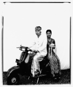 Indonesia, Bali, Ubud, Balinese wedding couple in ceremonial dress, sitting on motor scooter, woman carrying offering. - Martin Westlake