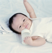 Baby girl, 9 months old holding milk bottle, smiling. - Erik Soh