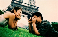 Young couple lying on grass, young woman posing for camera, smiling, Eiffel Tower in background. (high-grained) - Leila  Pivetta