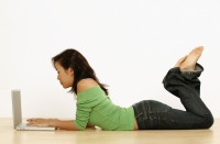 Young woman using laptop, lying on floor - Erik Soh