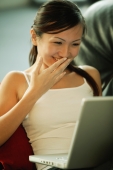 Young woman on sofa, using laptop, smiling - Alex Microstock02