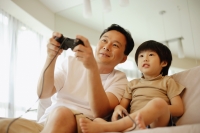Father and son sitting on sofa, playing with video game, low angle view - Alex Microstock02
