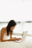 Young woman lying on bed, using laptop - Alex Microstock02