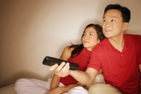 Man and woman sitting side by side, man holding remote control - Alex Microstock02