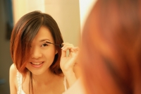 Woman putting on mascara, looking at mirror - Alex Microstock02