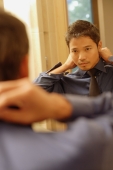 Young man adjusting tie and collar, looking in mirror - Alex Microstock02