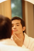 Young man  looking in mirror, touching his face - Alex Microstock02