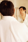 Young man touching his face, looking in mirror, rear view - Alex Microstock02
