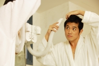 Young man blow drying hair, looking in mirror - Alex Microstock02