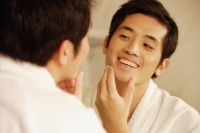 Young man touching his face, looking in mirror - Alex Microstock02