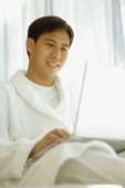 Young man wearing robe, using laptop - Alex Microstock02